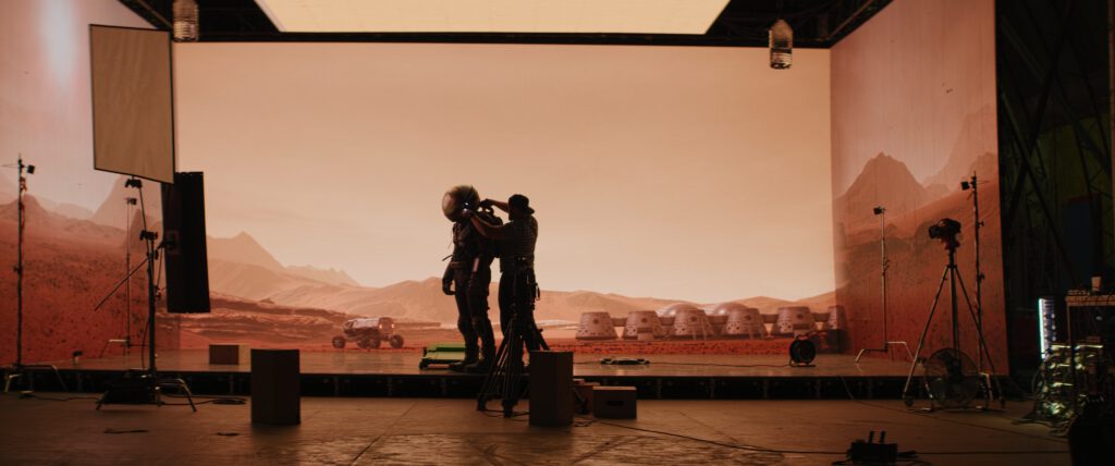 Diversität und ein Blick in die Zukunft - Behind the scenes shot of virtual production stage with huge LED screens, cinematorgapher shooting Mars scene. Future of movie production